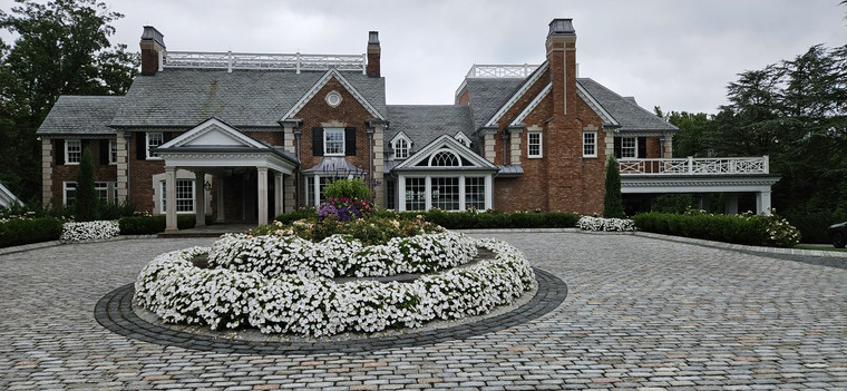 Cobblestone circular driveway with white floral center bed in front of a brick estate home