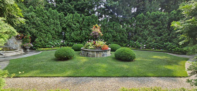 Formal garden lawn with stone planter centerpiece, boxwood spheres, and tall arborvitae