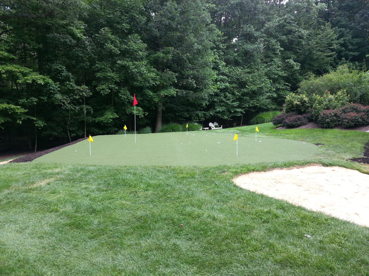 Large backyard putting green with sand bunker bordered by mature trees