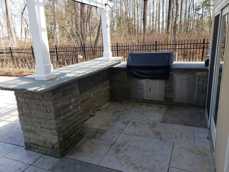 Covered stone outdoor kitchen with bar counter and built-in grill