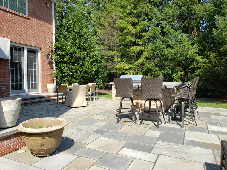 Bluestone patio with bar seating beside a brick home and tall evergreens