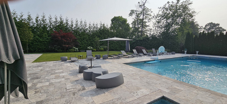 Travertine pool patio with lounge seating, umbrella, and manicured lawn
