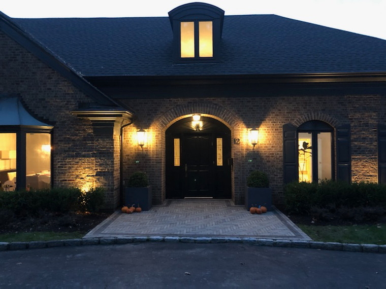 Brick estate entry with herringbone paver walkway and arched portico lit at dusk