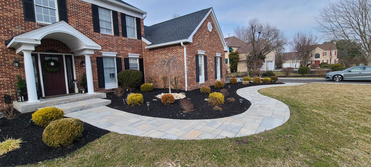 Curved bluestone walkway through fresh mulch beds and shrubs at a brick colonial