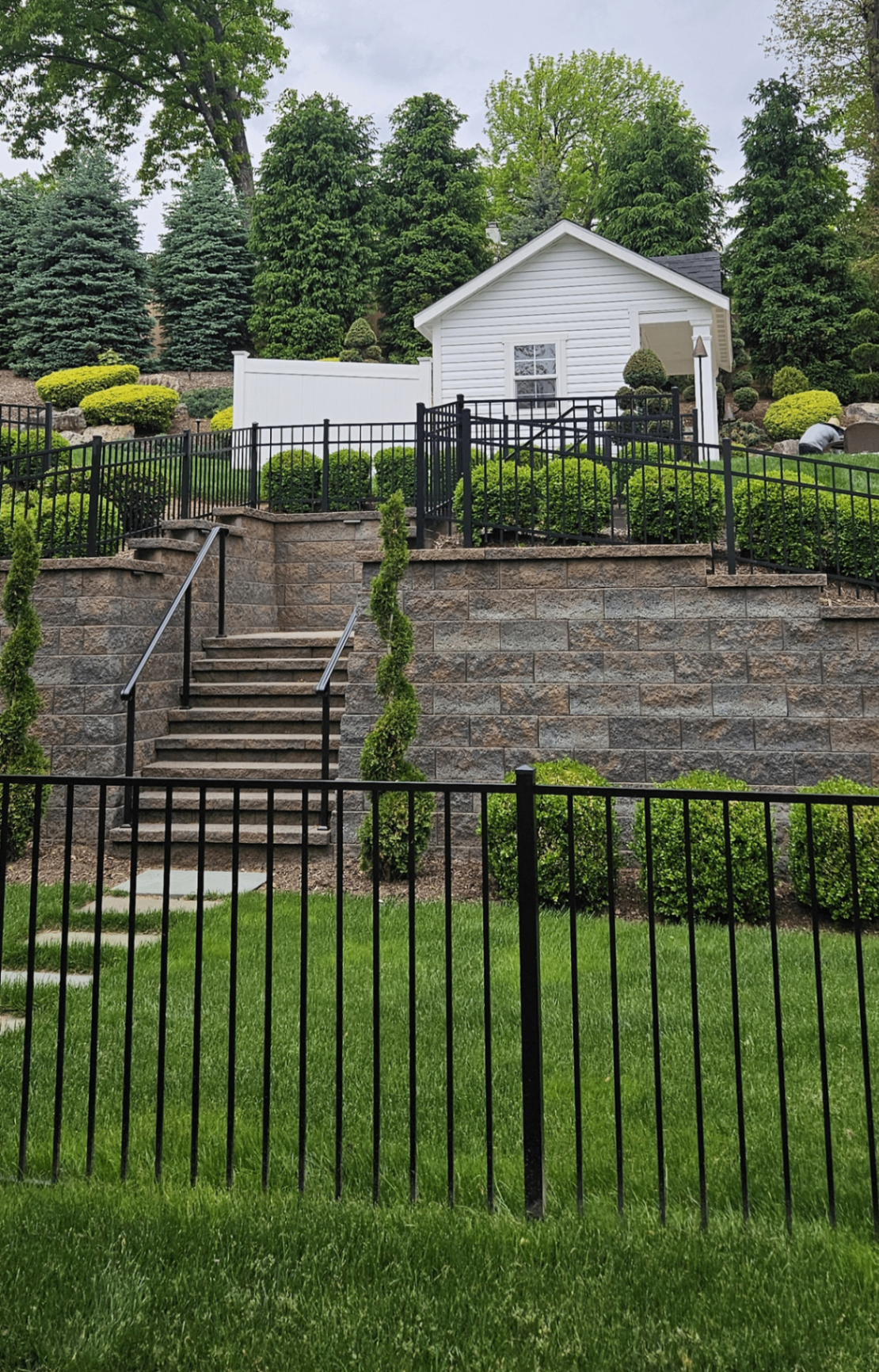 Tiered retaining wall with stone steps, manicured shrubs, and pool house above — Aaron's Landscape & Design