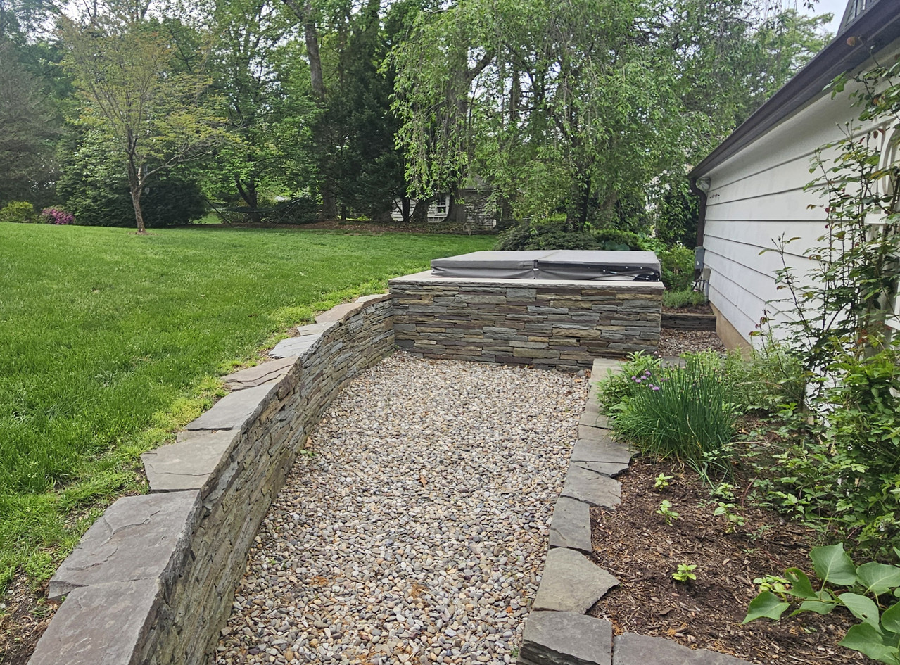 Curved natural stacked-stone wall enclosing a gravel patio with hot tub