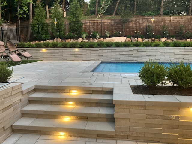 Lit stone pool surround with raised planter wall at dusk